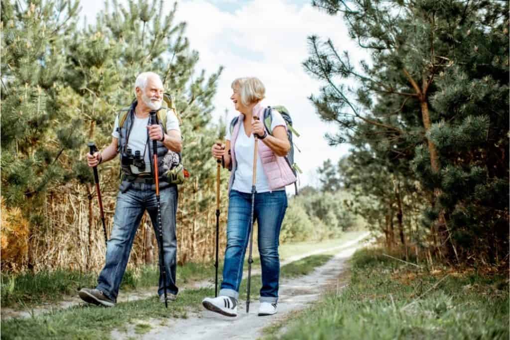 Midlife couple pursuing the health benefits of walking with poles along a track in the conifer forest