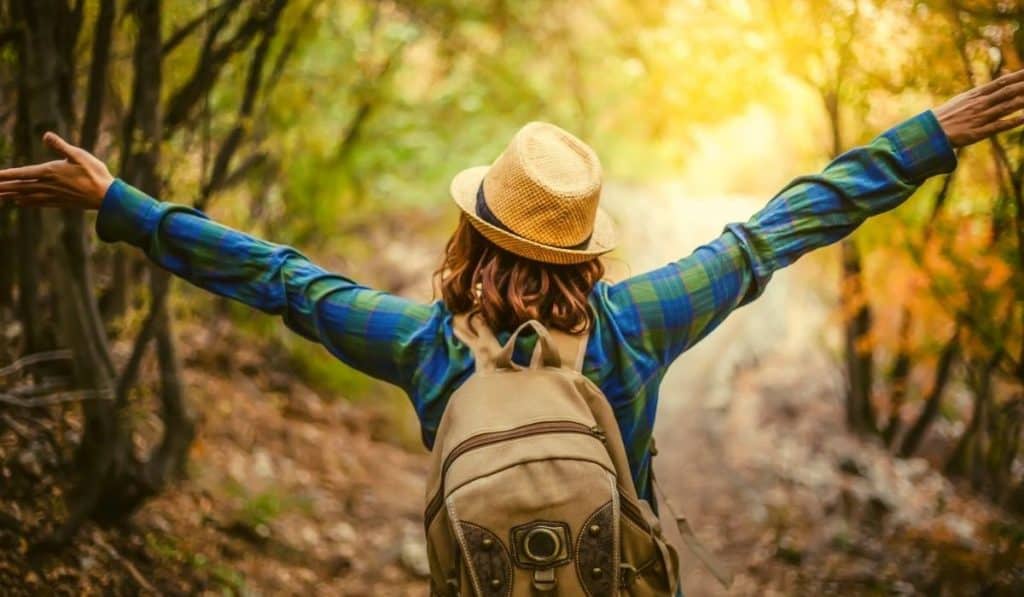 Woman walking in the wood with arms akimbo and her back to us but obviously elated from walking in nature