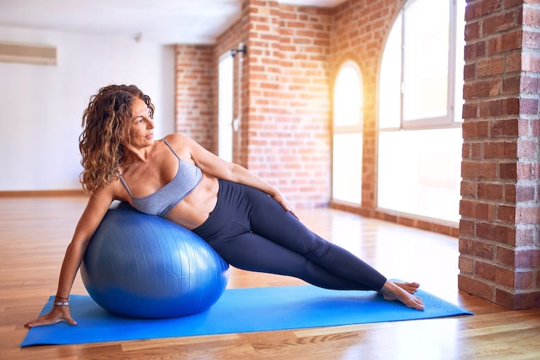 Midlife woman using an exercise ball in an empty room strengthening her lats